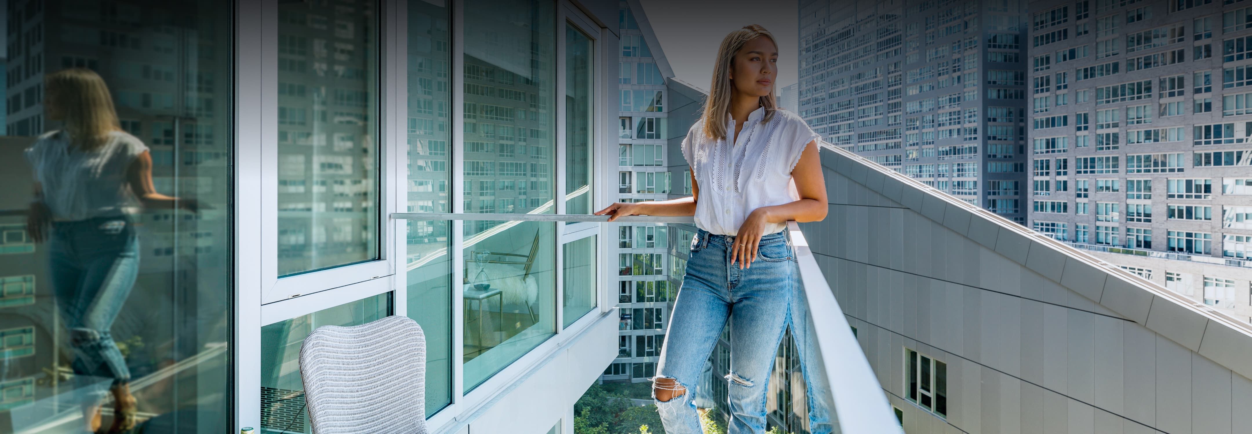 Woman on balcony with cityscape reflection, casual style, high-rise background.