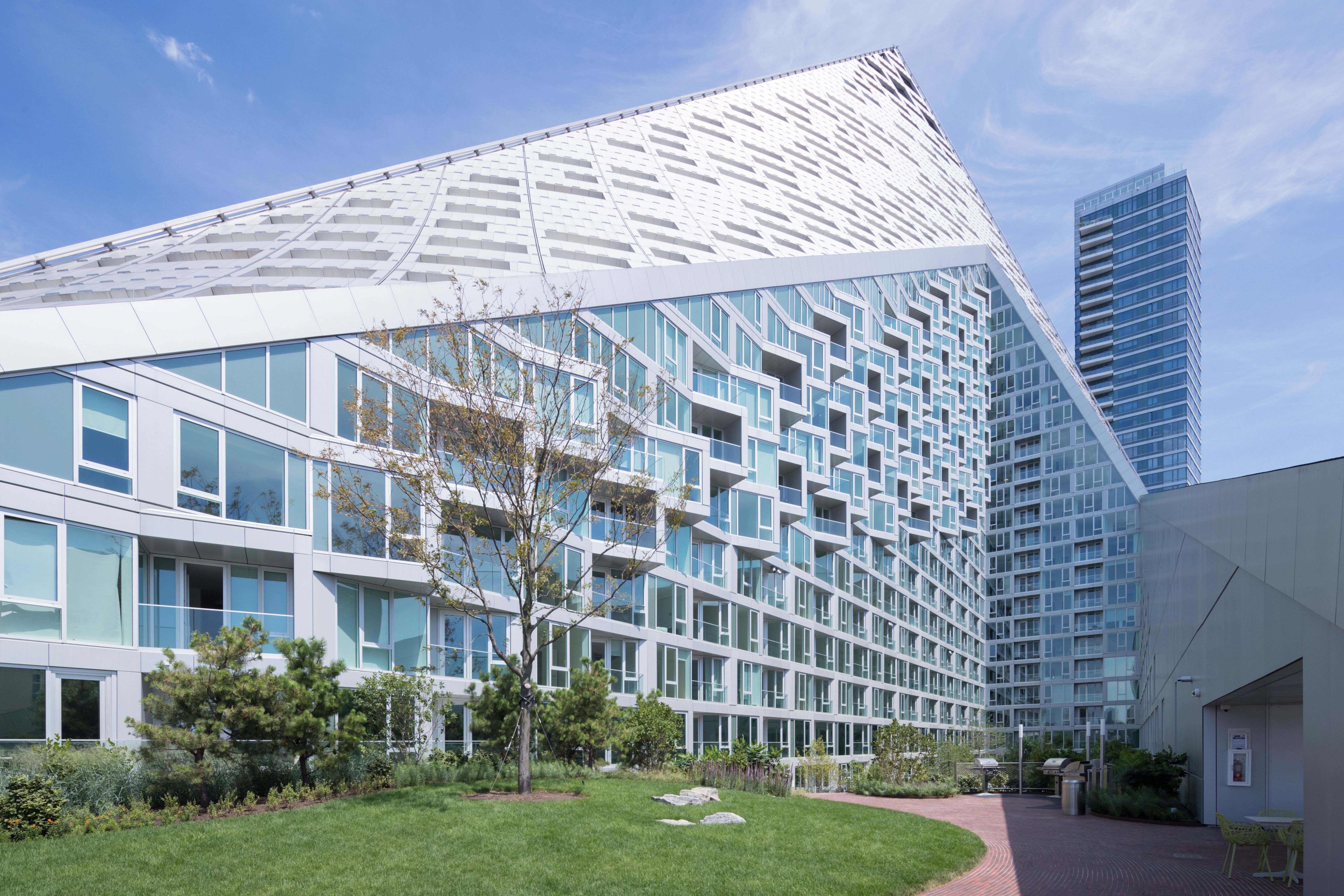 Modern white angular building with unique balconies, nestled in a lush green park.