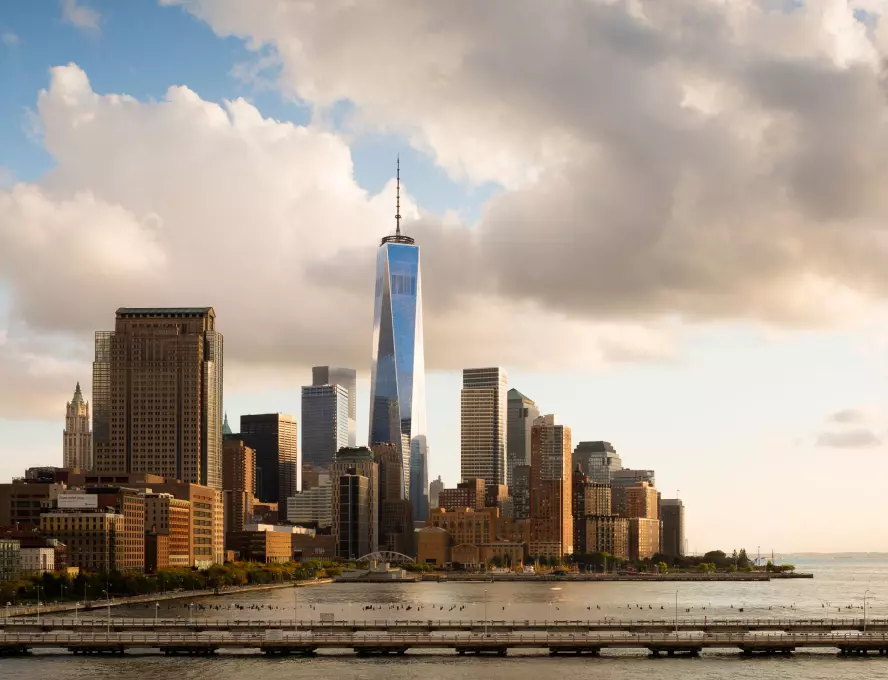 Lower Manhattan skyline with prominent skyscraper and Hudson River in the foreground.