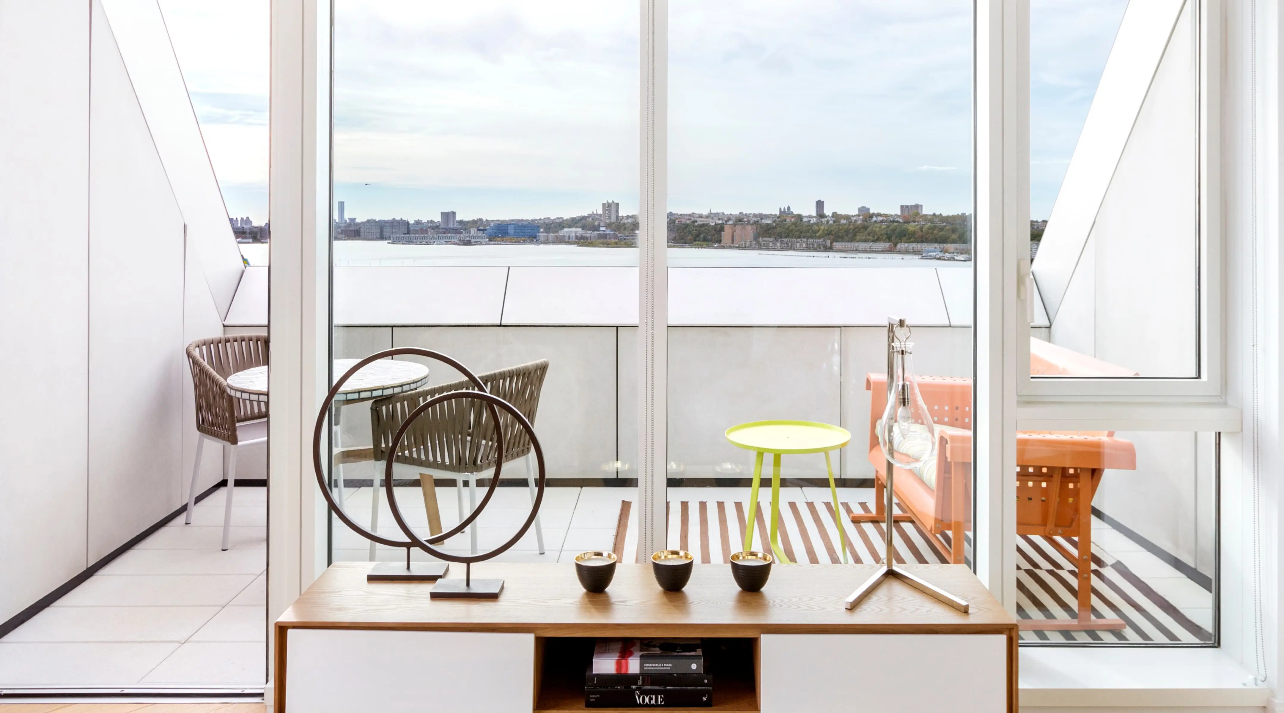 Chic terrace with a river view, green table, wicker chairs, and art piece.